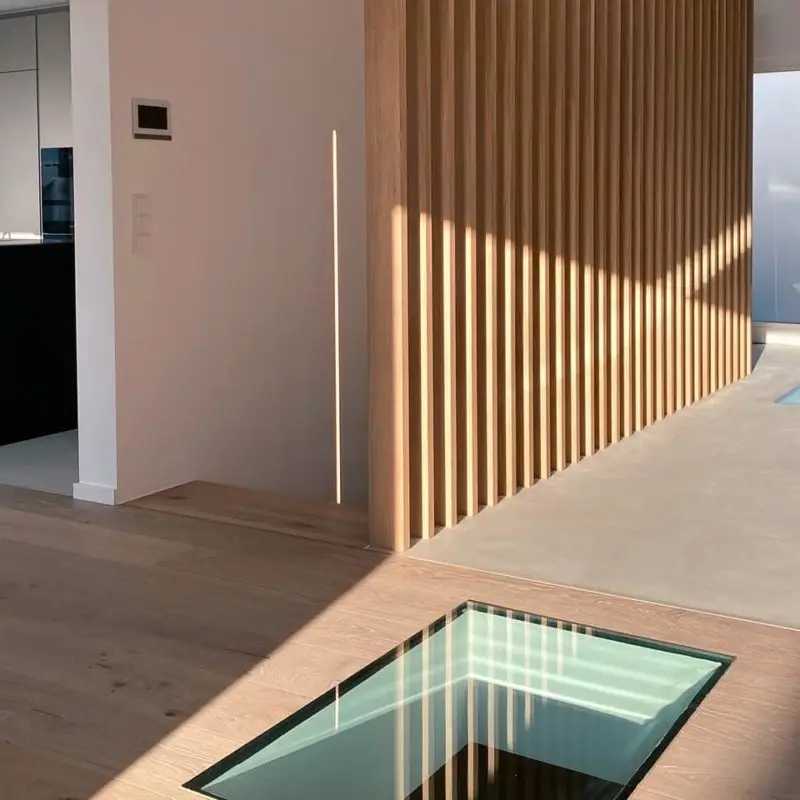 Moderner Wohnbereich im GERBERHAUS6 mit elegantem Glasboden und dekorativer Holzlamellen, die den Flur von der Treppe trennt.