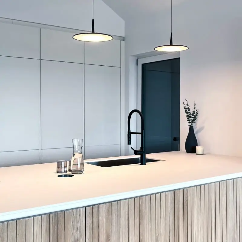 Küche mit weißer Kochinsel, Holzfronten, schwarzem Wasserhahn und zwei modernen Hängeleuchten.