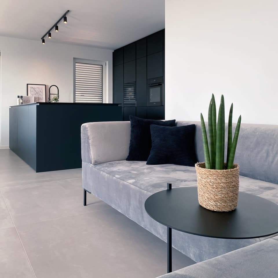 Wohnbereich mit grauem Sofa, schwarzer Beistelltisch, Blick auf schwarze Küche mit Fenix Arbeitsplatte