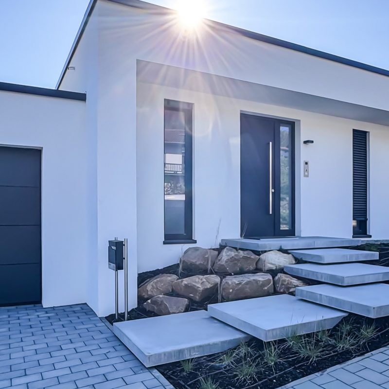 Außenaufnahme von #GERBERHAUS16 mit minimalistischer Architektur, schwebenden Betonstufen und Sonnenlicht über dem Walmdach