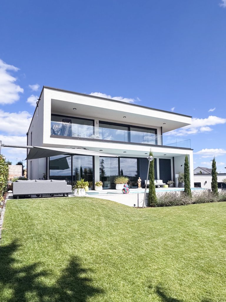 GERBERHAUS12 von der Gartenseite: moderne Villa mit Flachdach, großen Glasfronten, Glasbalustrade, Pool und Rasen