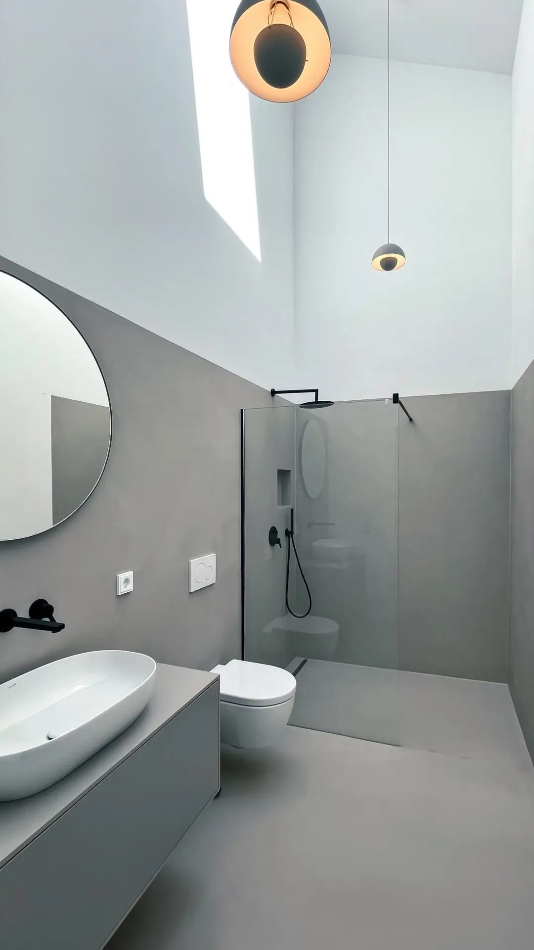 Zeitgemäßes Badezimmer im GERBERHAUS8 mit fugenlosem Mikrozement, einer großen Dusche und natürlichem Tageslichteinfall durch ein Oberlicht.