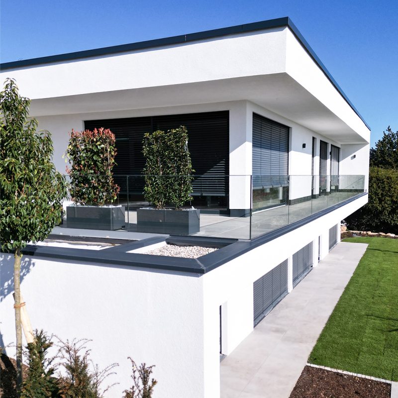 Seitliche Hausansicht von #GERBERHAUS16 mit umlaufender Terrassenebene, Glasgeländer und angelegtem Garten