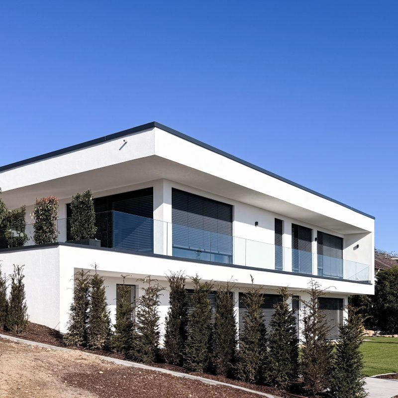 Modernes Einfamilienhaus in Hanglage mit Flachdach, großen Glasflächen und umlaufendem Balkon, minimalistische Architektur und Außenanlagen bei #GERBERHAUS16