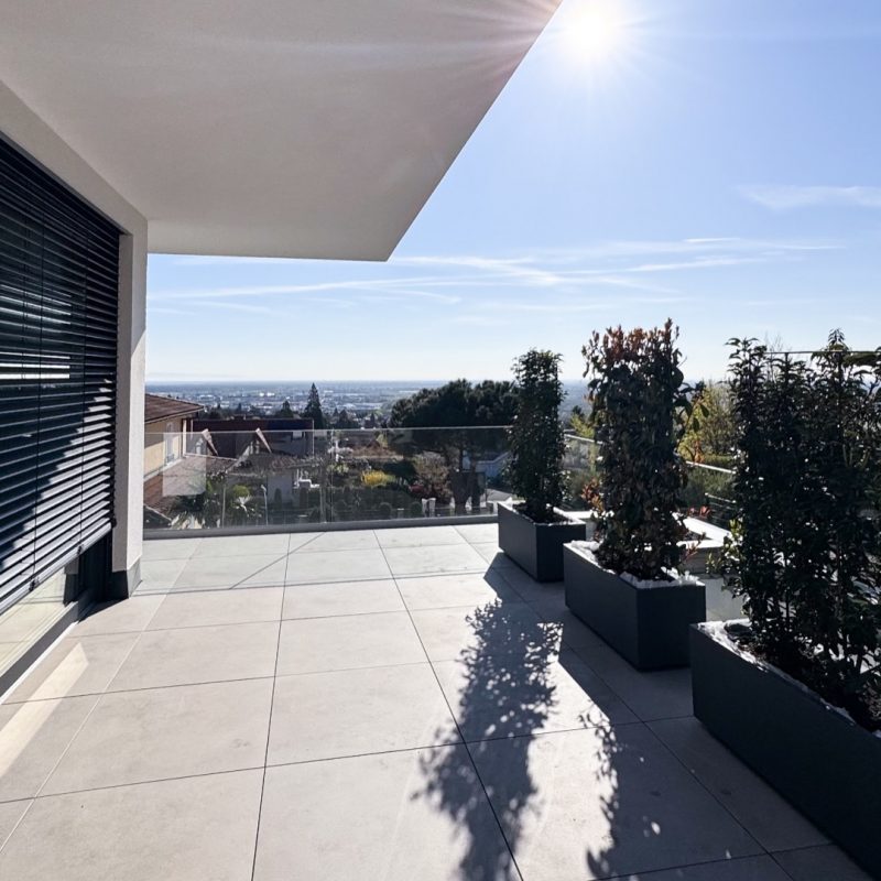 Großzügige Dachterrasse mit Glasgeländer, Pflanzkübeln und Sonneneinstrahlung, moderne Architektur mit überdachtem Bereich und weitem Ausblick – Einfamilienhaus #GERBERHAUS16