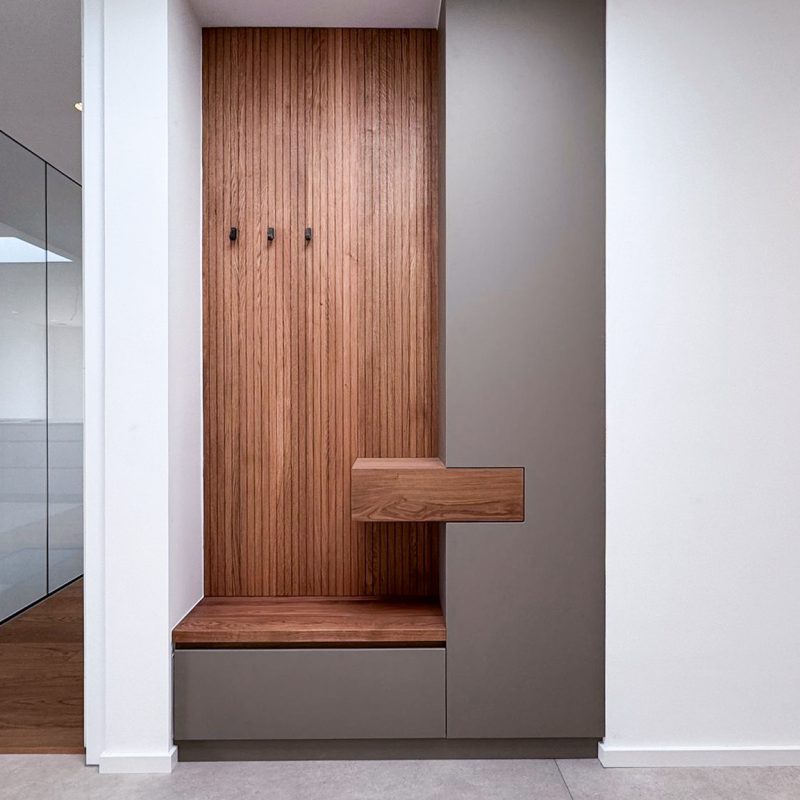 Garderobe im #GERBERHAUS16 mit vertikaler Lamellenrückwand aus Holz, Sitzbank und geschlossenen Stauraum-Elementen in matten Fronten.