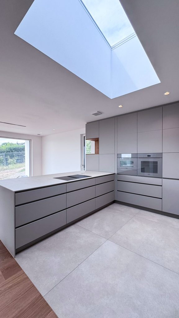 Moderne offene Küche mit Kochinsel, Dachfenster und Miele Geräten in Pearl Beige, grifflose Küchenfronten und minimalistisches Design in #GERBERHAUS16