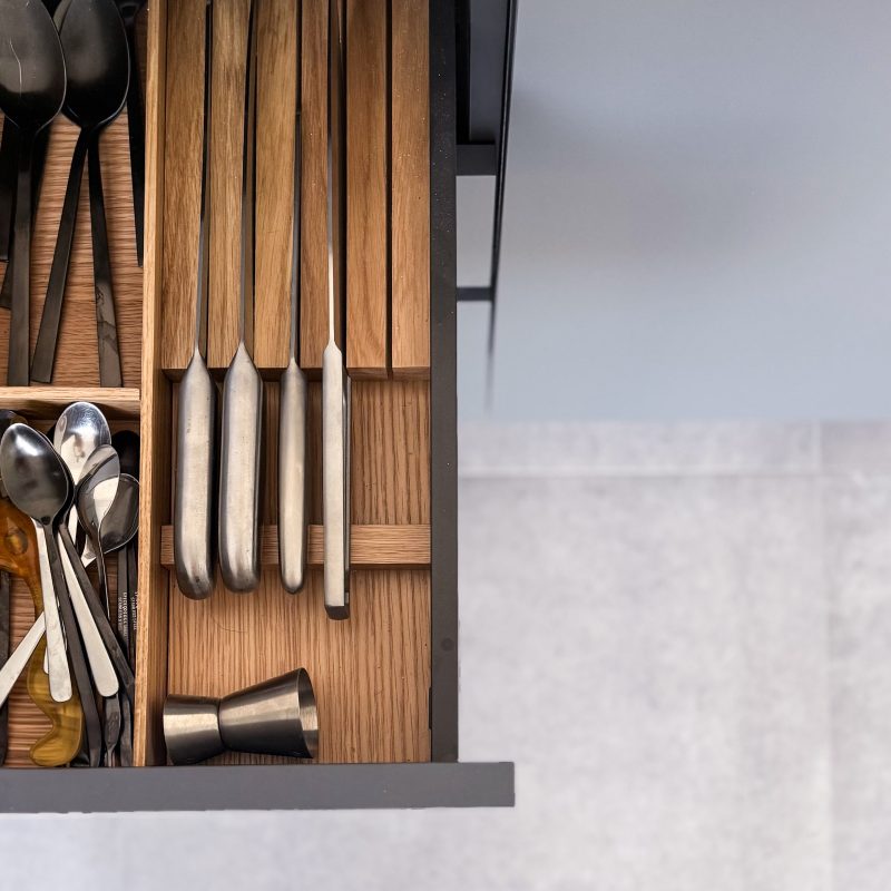 Offene Besteckschublade mit maßgefertigtem Holzeinsatz aus Eiche für Messer und Löffel in der modernen Küche des Umbaus U06.