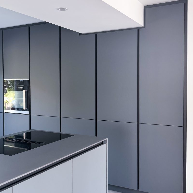 Detailansicht der modernen Küche im Umbau U06 mit grifflosen, schwarzgrauen Fronten, Kücheninsel mit Induktionskochfeld und großen Schrankflächen.