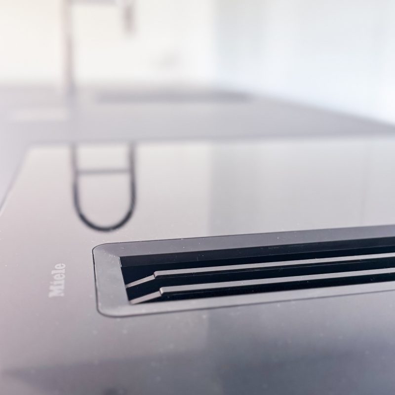 Detailaufnahme eines Miele-Induktionskochfelds mit integriertem Dunstabzug im Umbau U06, im Hintergrund unscharf die Küchenarmatur.