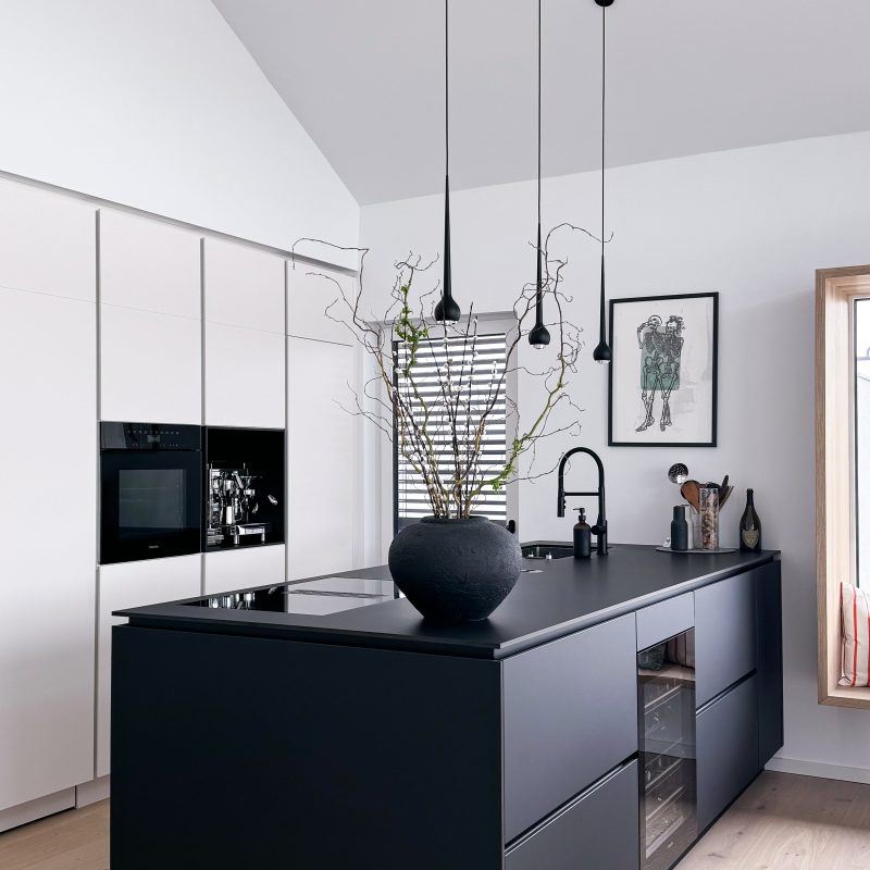 Moderne Küche von Gerber Ingenieure mit schwarzer Kücheninsel, integrierten Geräten, hängenden Pendelleuchten und dekorativer Vase.