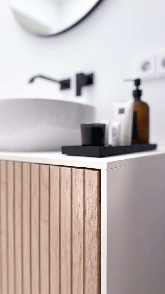 Nahaufnahme eines modernen Waschtischs mit Holzverkleidung, rundem Spiegel und minimalistischer Dekoration.