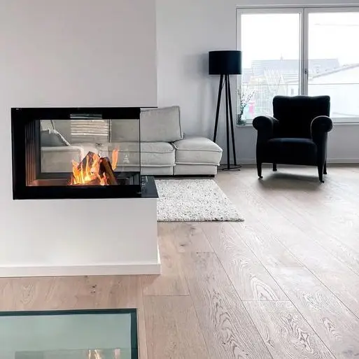 Wohnzimmer mit weißem minimalistischen Kamin in dem ein Feuer brennt. Eichenparkettboden mit eingelassenem Bodenfenster