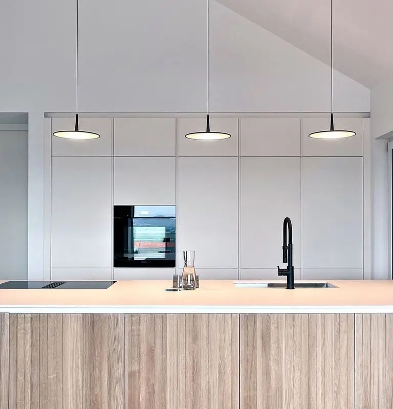 Küche mit weißem Einbauschrank und moderner Kochinsel aus Holz, beleuchtet von stilvollen Hängeleuchten.