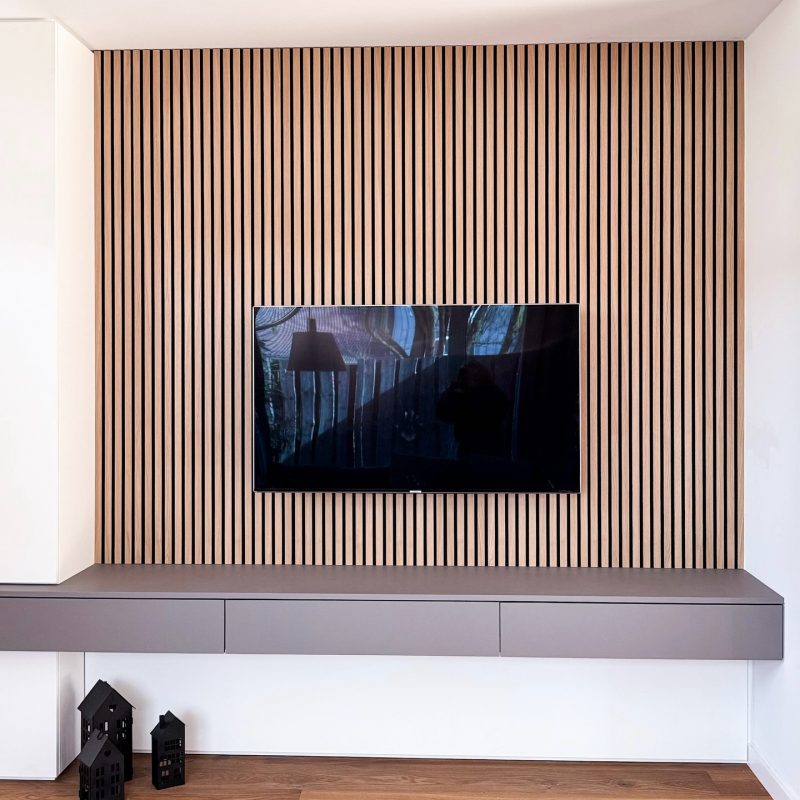 Moderne TV-Wand mit vertikalen Holzlamellen und schwebendem Lowboard, minimalistischer Innenausbau mit klarer Linienführung aus der Schreinerei