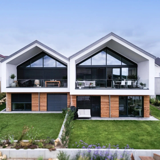 Foto der fertiggestellten Doppelhaushälften #GERBERHAUS10A & 10B in Alzey mit großen Glasfronten, überdachten Balkonen und Holzfassadenelementen.