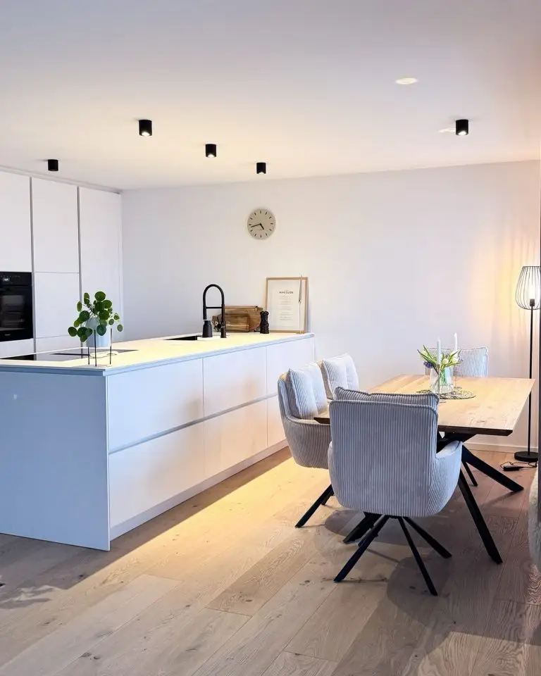 Helle Wohnküche mit weißer Kochinsel, integrierter Spüle, Designerstühlen und Holztisch auf Eichenparkett