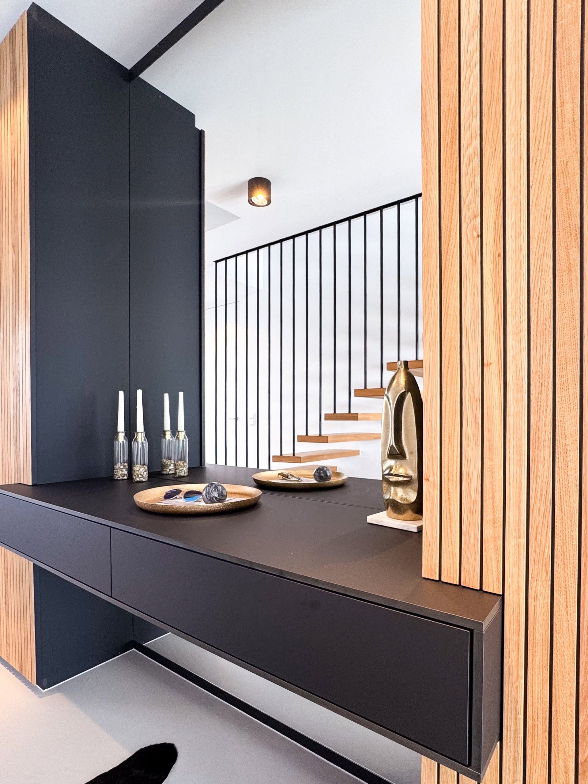 Maßgefertigte Garderobe im Eingangsbereich des GERBERHAUS12: schwarze grifflose Schrankfronten, schwebende Konsole und Eichenlamellen