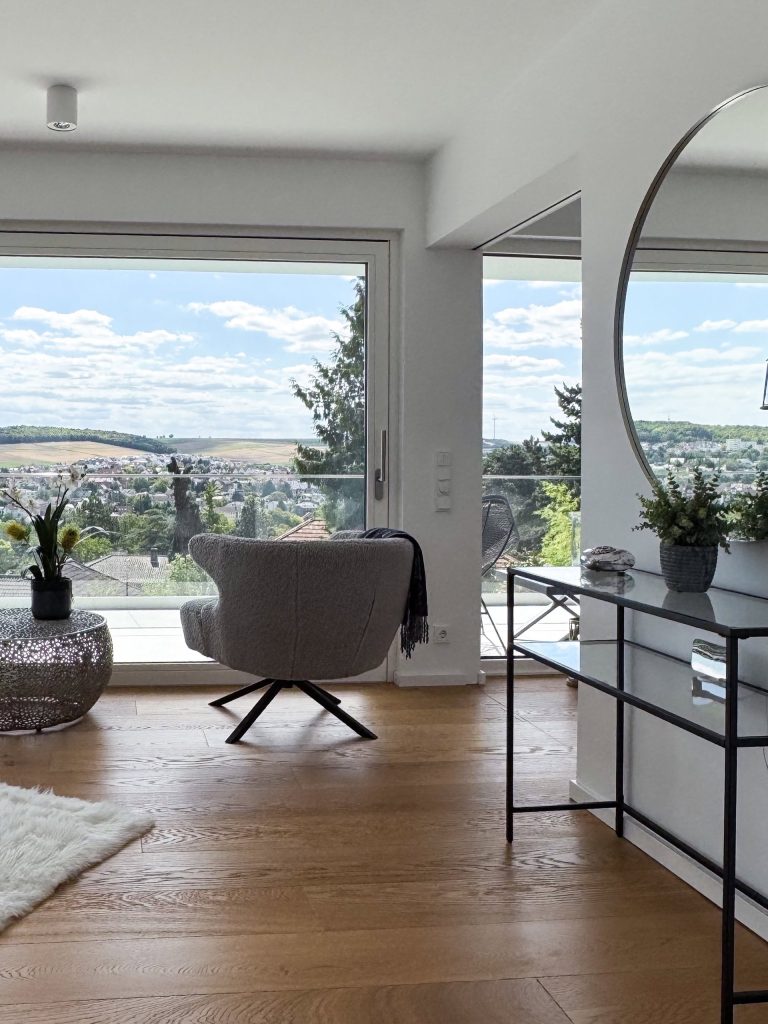 Raumhohes Panoramafenster im GERBERHAUS12 mit Sessel auf Holzboden und weitem Blick über die Landschaft