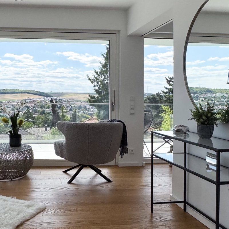 Raumhohes Panoramafenster im GERBERHAUS12 mit Sessel auf Holzboden und weitem Blick über die Landschaft