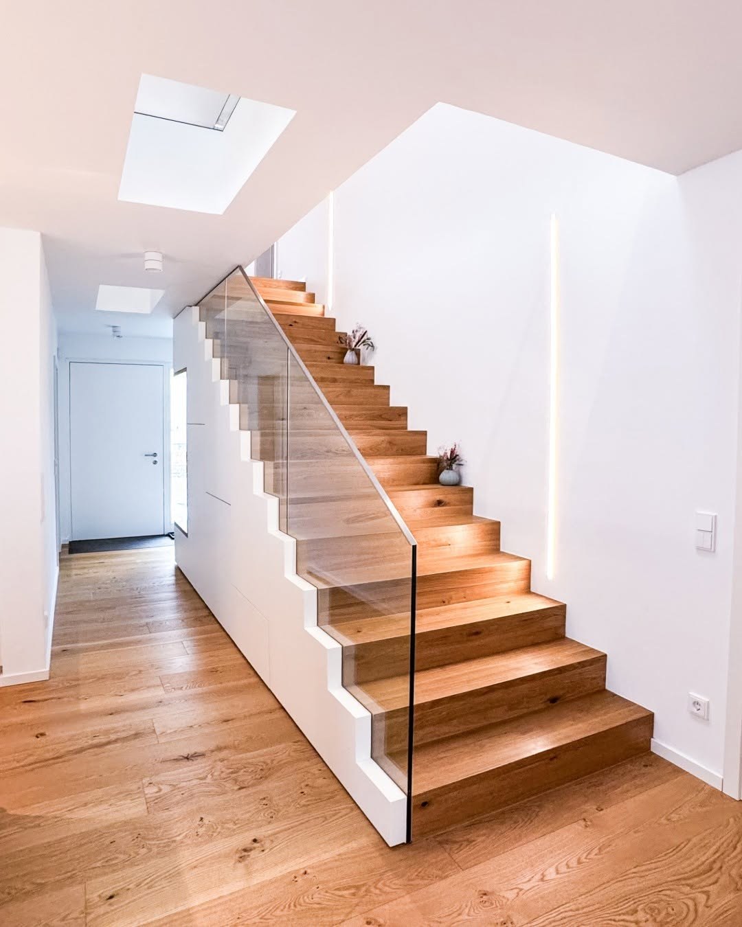 Treppe mit Stufen aus Eiche, rahmenlosem Glasgeländer, weißen Einbauschränken darunter und senkrechter LED-Lichtleiste im GERBERHAUS15