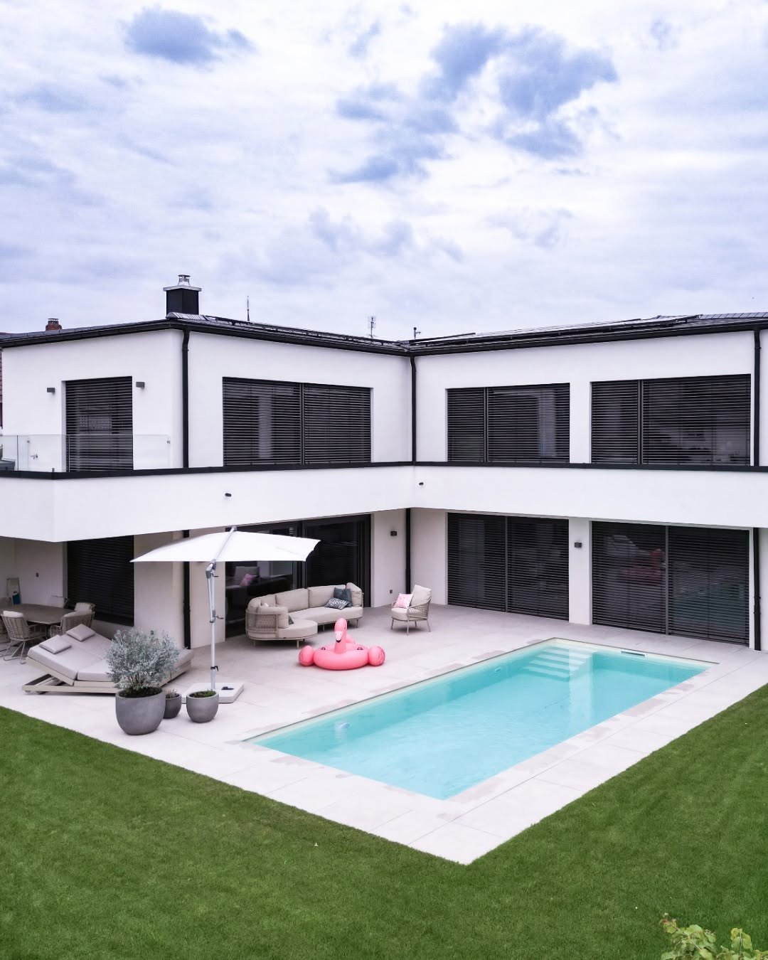 GERBERHAUS15 von oben: Einfamilienhaus in L-Form mit weißer Putzfassade, Terrasse mit Lounge, Pool und Rasen